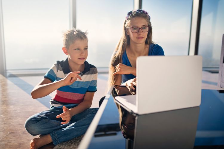 Zwei Kinder sitzen vor einem Laptop mit einer barrierefreien Website und kommunizieren in Zeichensprache